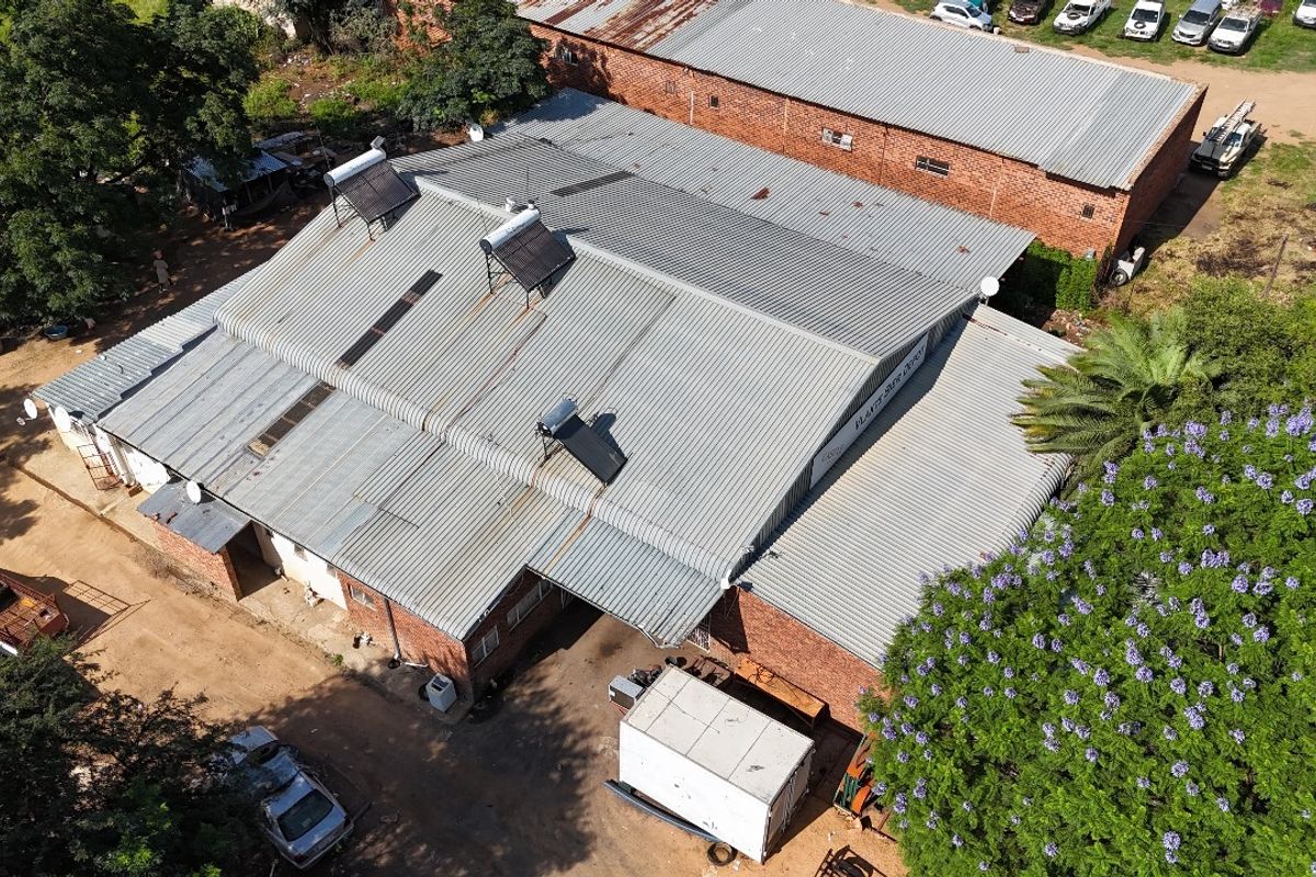 Aerial view of an industrial warehouse property featuring a large corrugated metal roof with multiple solar water heating units installed.