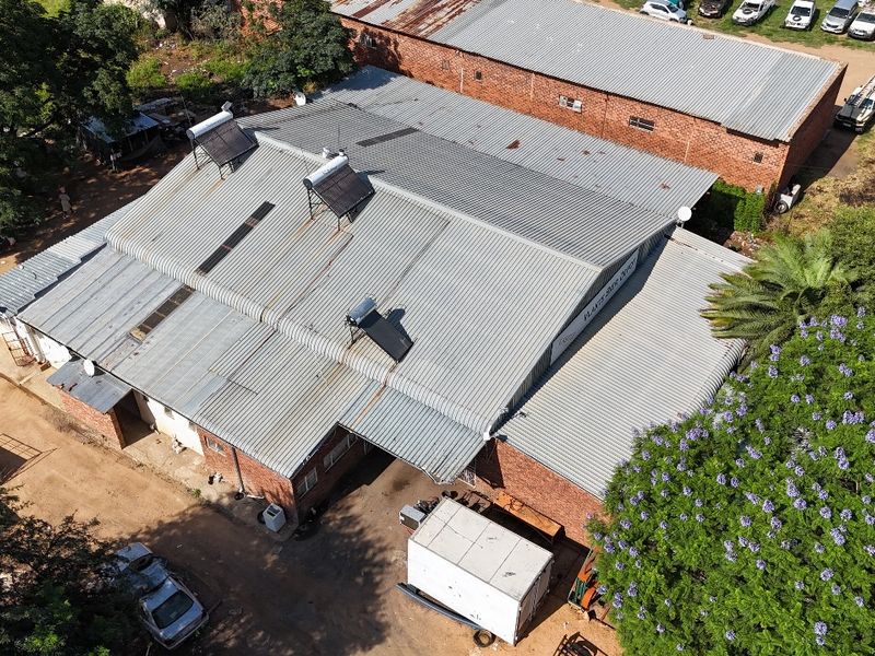 Aerial view of an industrial warehouse property featuring a large corrugated metal roof with multiple solar water heating units installed.