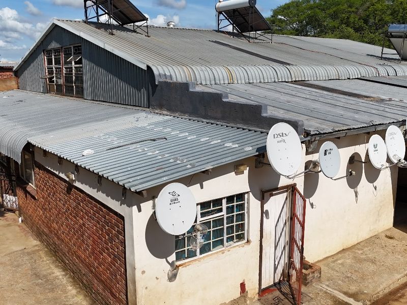 Aerial view of an industrial-style building featuring a corrugated metal roof with solar water heaters and brick and plaster exterior walls.