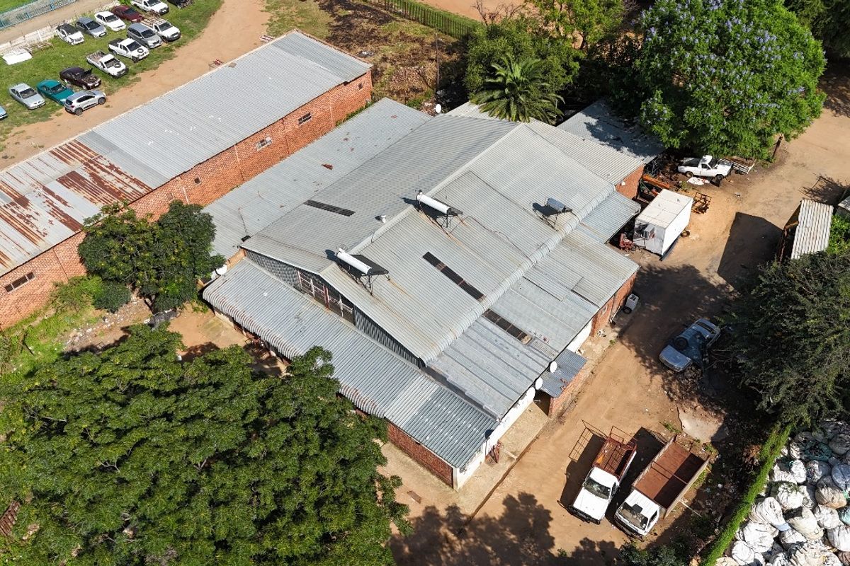 Aerial view of an industrial property featuring multiple corrugated metal roof structures, solar water heating units, and surrounding yard space.