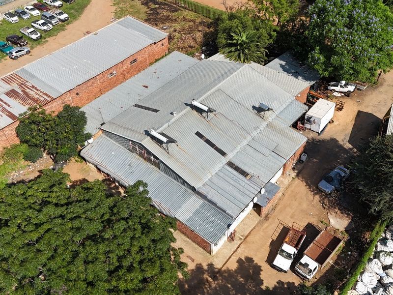 Aerial view of an industrial property featuring multiple corrugated metal roof structures, solar water heating units, and surrounding yard space.