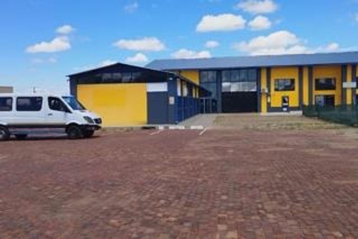 Front exterior view of an industrial property featuring a paved parking area, metal cladding, and a large roller shutter door.