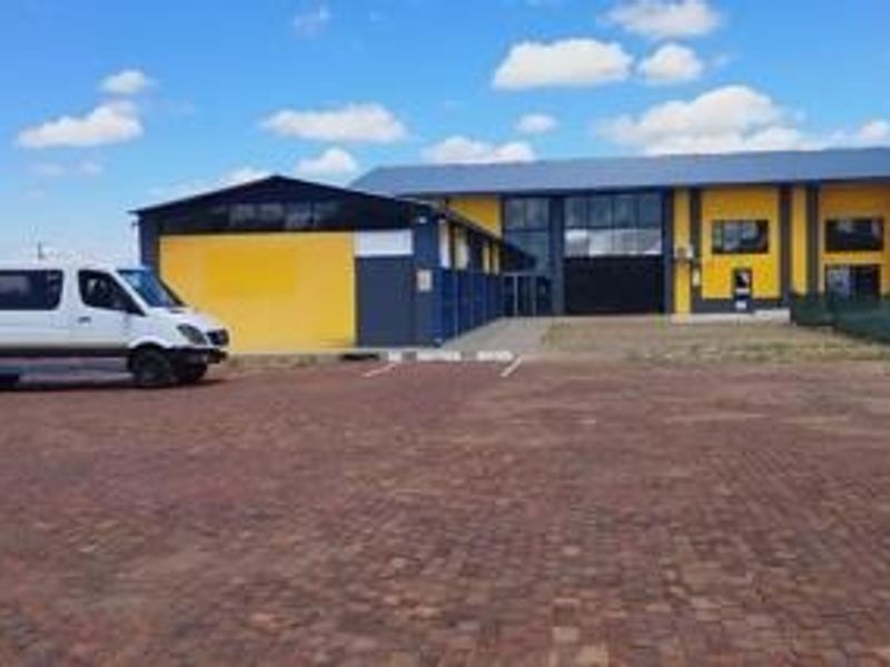 Front exterior view of an industrial property featuring a paved parking area, metal cladding, and a large roller shutter door.