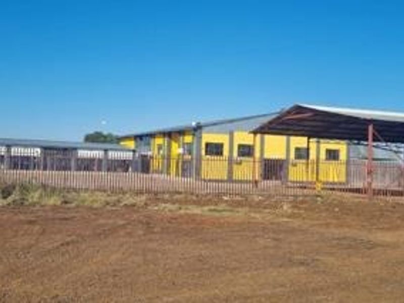 Industrial property featuring a warehouse building with metal roofing, enclosed by perimeter fencing and including a covered parking area.