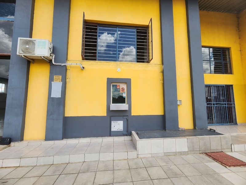 Exterior view of an industrial building facade featuring a service window, security safe, air conditioning unit, and tiled entrance area.