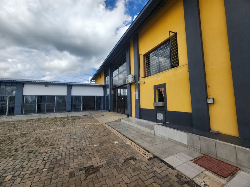 Exterior view of an industrial property featuring a paved driveway, security gates, and a service window, showing signs of wear on the exterior surfaces.