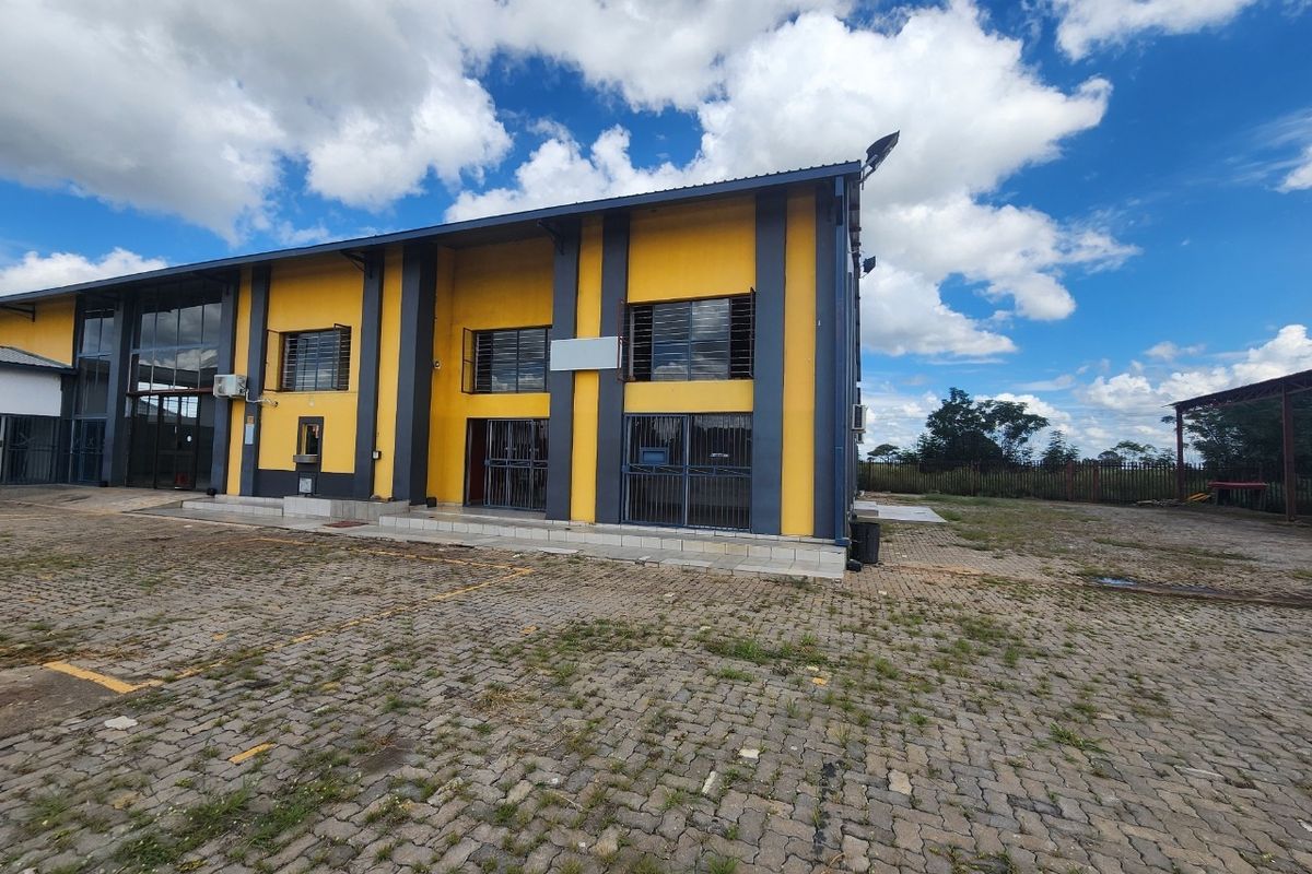 Industrial property exterior featuring a paved yard, metal security grilles on windows, and a prominent yellow and grey facade.