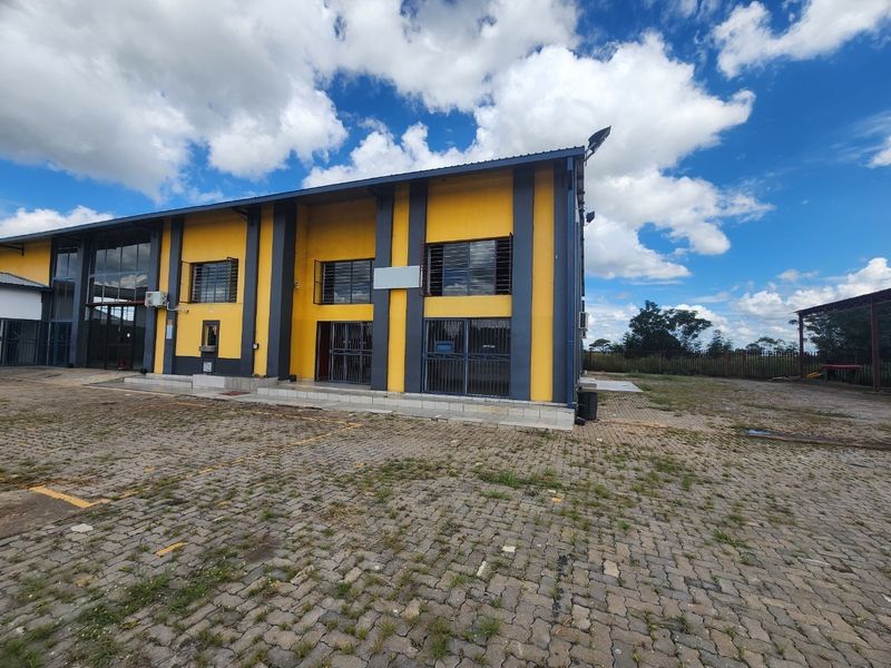 Industrial property exterior featuring a paved yard, metal security grilles on windows, and a prominent yellow and grey facade.