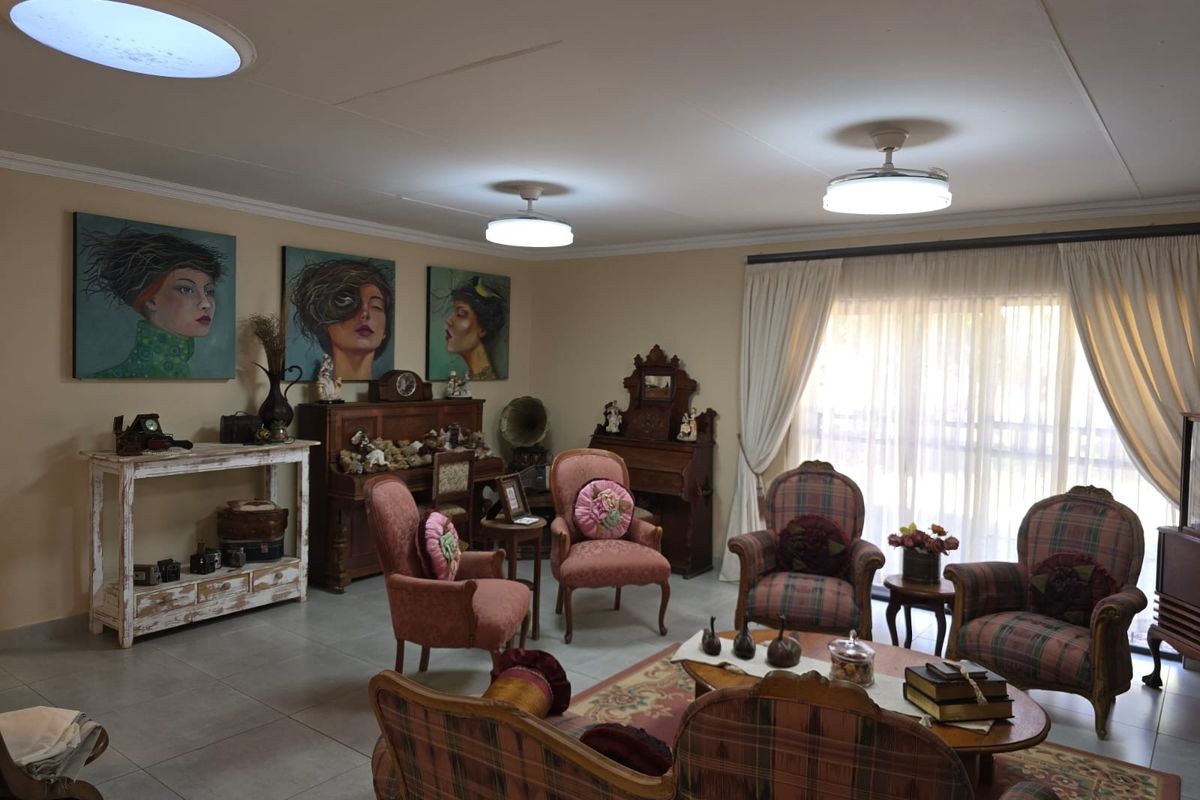 A spacious living room featuring tiled flooring, dual skylights, ceiling fans, and large sliding glass doors providing natural light.