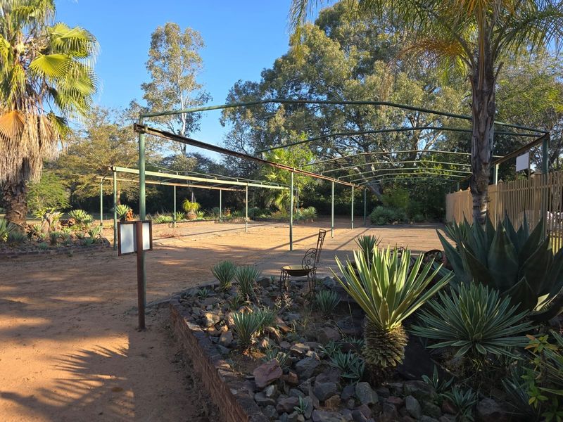 An expansive outdoor garden area featuring a large, weathered metal frame structure and established rock-bordered garden beds with various succulents.
