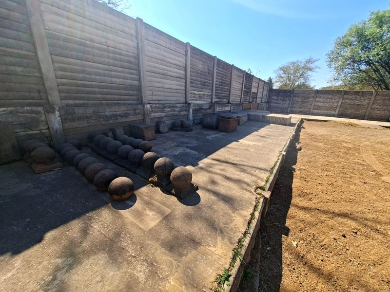 Rear exterior area featuring a large precast concrete boundary wall and a concrete paved section with adjacent unpaved ground.
