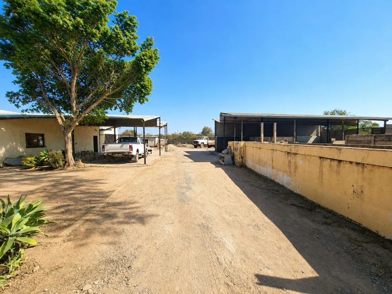 Industrial yard area featuring a large unpaved driveway, covered storage structures, and a perimeter concrete boundary wall.
