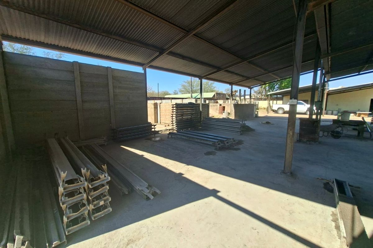 Open-plan industrial utility space featuring a corrugated metal roof, steel support columns, and durable concrete flooring, suitable for storage or workshop operations.