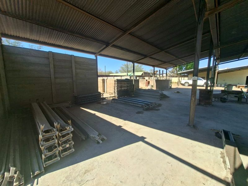 Open-plan industrial utility space featuring a corrugated metal roof, steel support columns, and durable concrete flooring, suitable for storage or workshop operations.