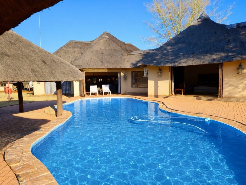 A well-maintained outdoor pool area featuring a swimming pool, brick paving, and traditional thatched roof structures with open-plan access to the main lodge.