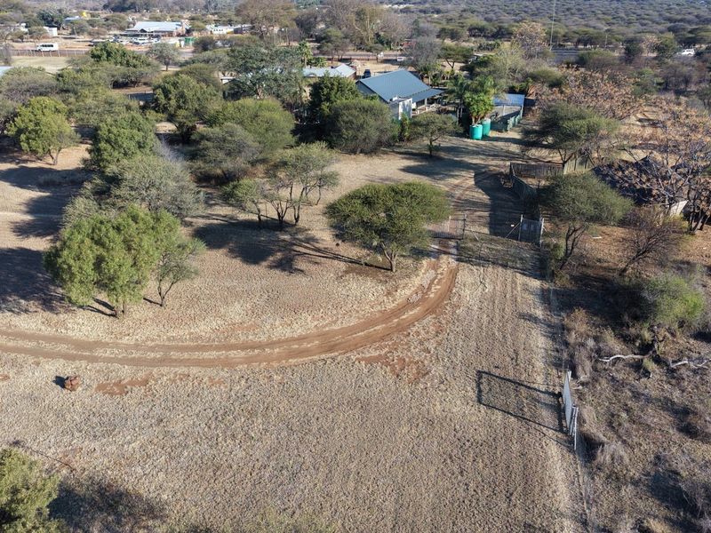 Aerial view of the lodge property featuring a dirt driveway, natural bushveld landscape, perimeter fencing, and existing building structures.