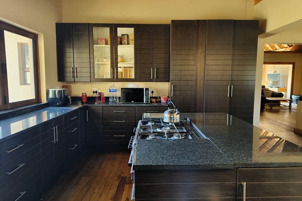A well-appointed kitchen featuring dark wood cabinetry, granite countertops, a central island with a gas hob, and a traditional thatched roof ceiling.