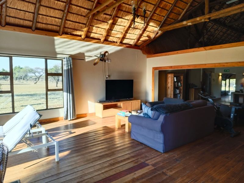 Spacious living area featuring a traditional thatched roof with exposed timber rafters, warm timber flooring, and large windows offering scenic views.