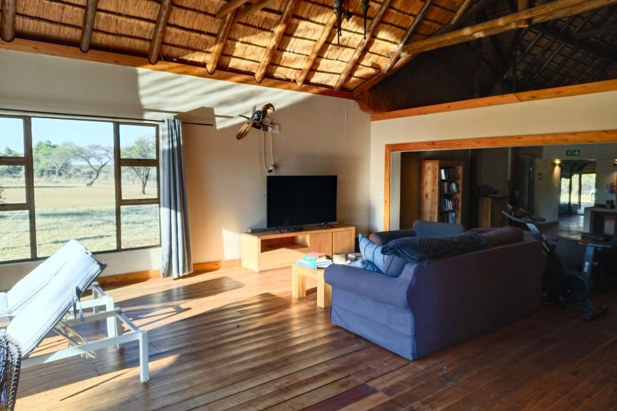 Spacious living area featuring a traditional thatched roof with exposed timber rafters, warm timber flooring, and large windows offering scenic views.