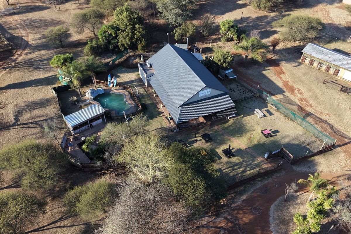 Aerial view of the lodge property featuring a main building with a metal roof, a swimming pool, and surrounding outdoor grounds.