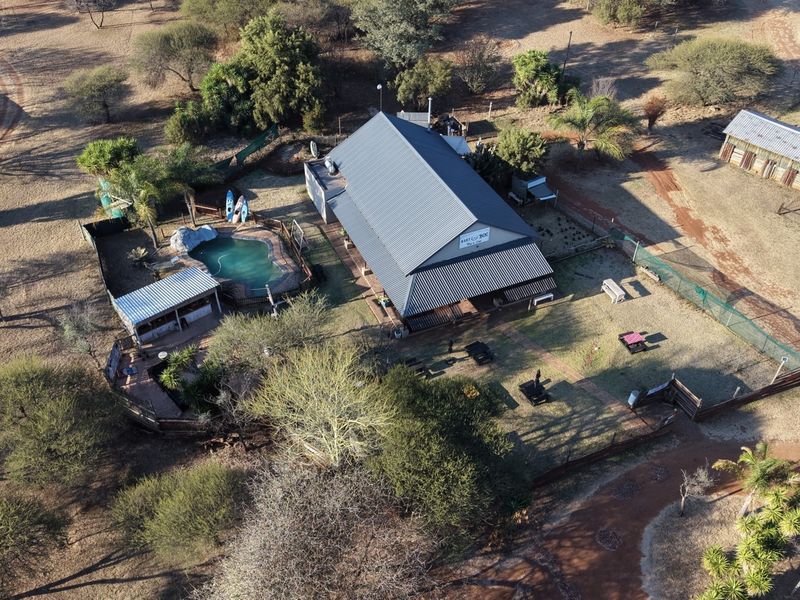 Aerial view of the lodge property featuring a main building with a metal roof, a swimming pool, and surrounding outdoor grounds.