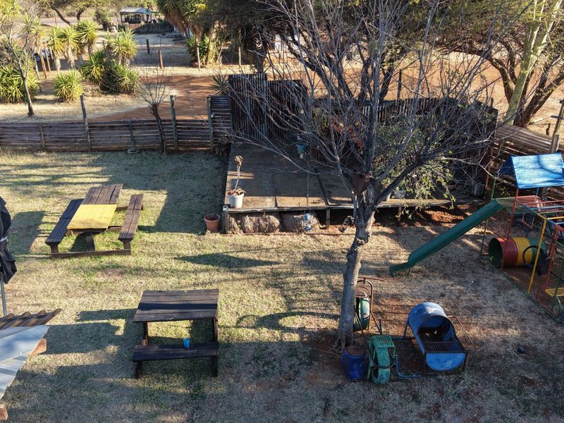 An elevated view of a rear garden area featuring a wooden deck, perimeter fencing, and a children's play area with a slide.