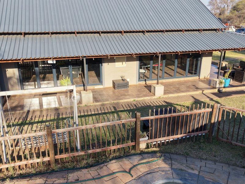 Aerial view of the rear exterior featuring a large covered patio with sliding glass doors, corrugated metal roofing, and a fenced garden area.