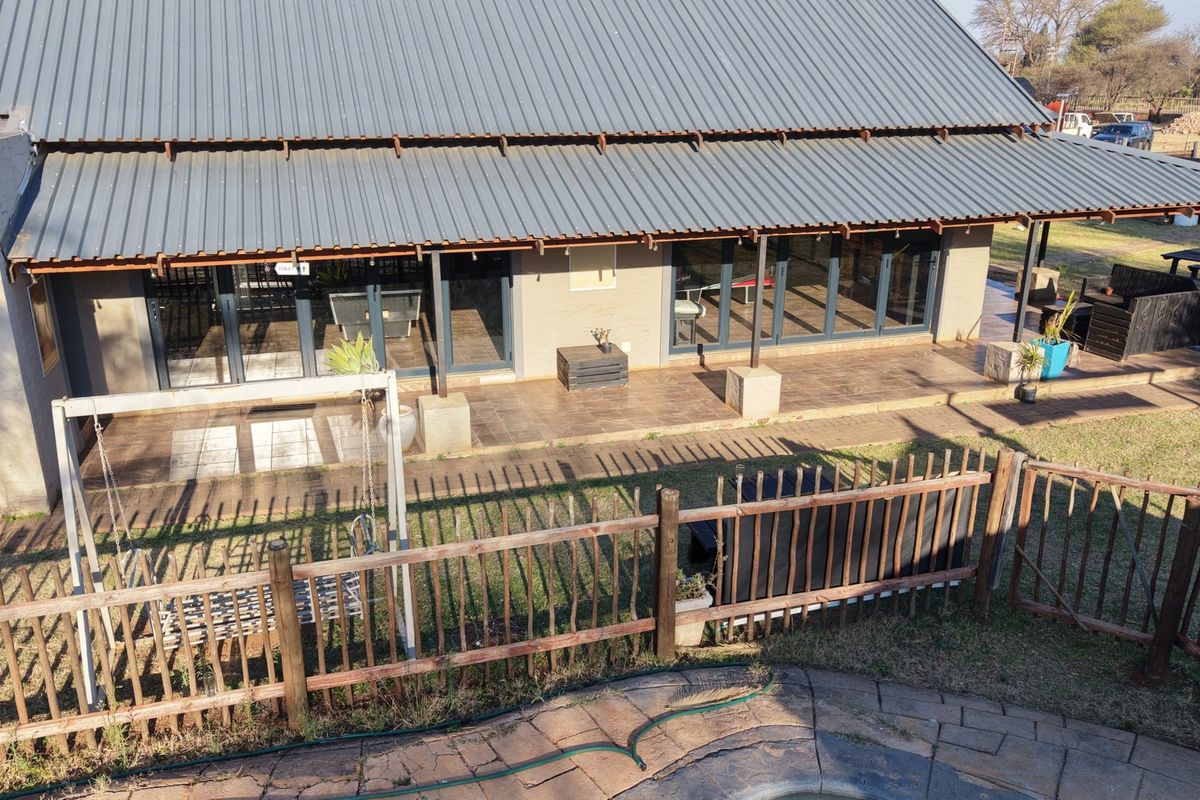 Aerial view of the rear exterior featuring a large covered patio with sliding glass doors, corrugated metal roofing, and a fenced garden area.