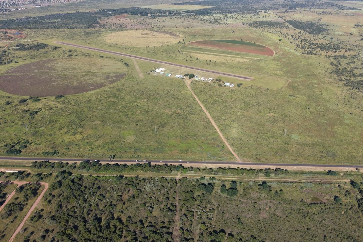 Aerial view of a large commercial vacant land plot featuring an existing airstrip, access road, and surrounding natural landscape.