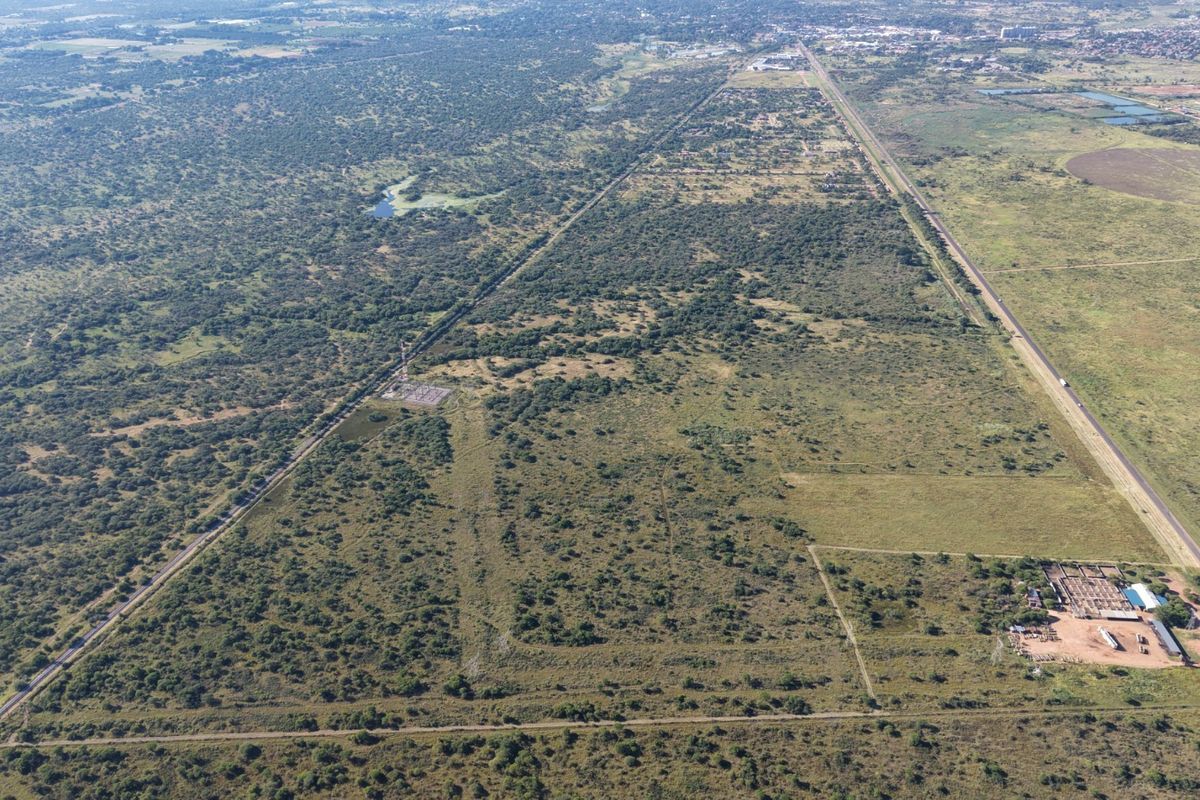Aerial view of a large, undeveloped commercial land parcel featuring natural vegetation, access roads, and existing power infrastructure.