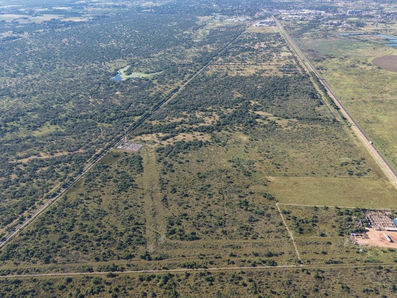 Aerial view of a large, undeveloped commercial land parcel featuring natural vegetation, access roads, and existing power infrastructure.