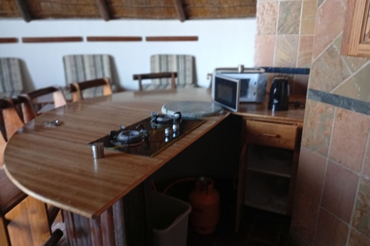 A dated kitchen area featuring a built-in gas hob, wooden cabinetry, and a traditional thatch roof ceiling.