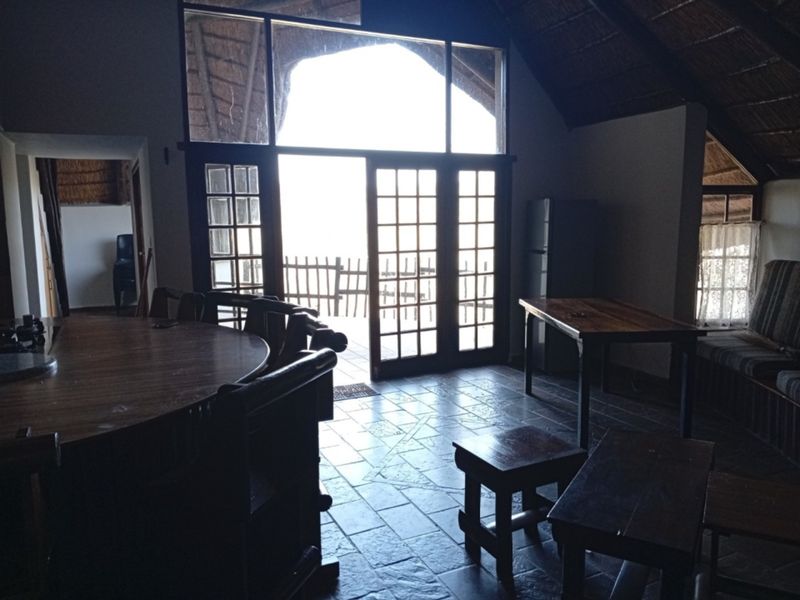 Open-plan living area featuring a high thatched ceiling with exposed rafters, tiled flooring, and large french doors leading to an outdoor space.