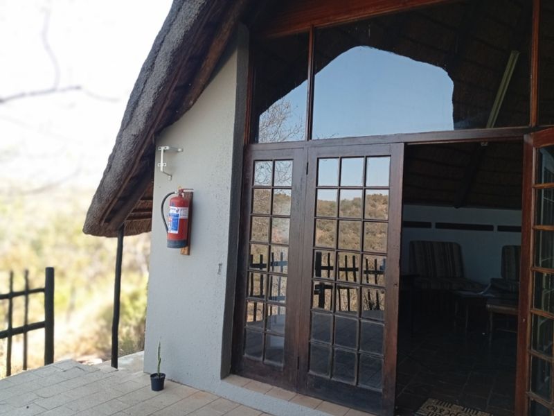 Exterior view of a thatched roof apartment featuring timber-framed glass doors opening onto a paved patio area.