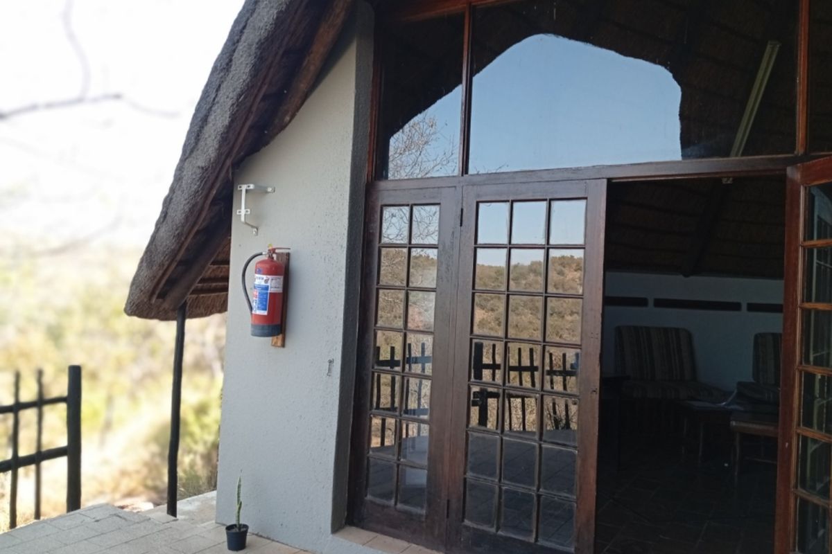 Exterior view of a thatched roof apartment featuring timber-framed glass doors opening onto a paved patio area.