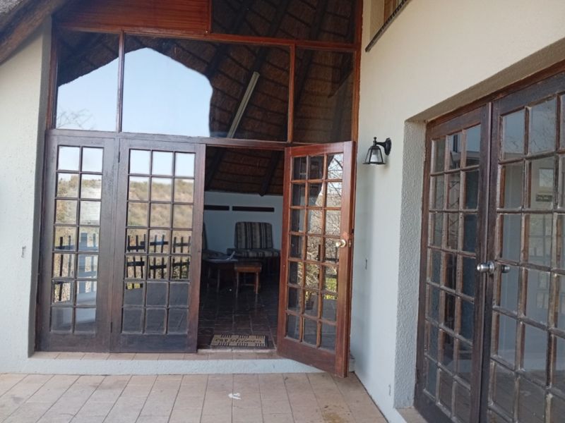 Covered patio area featuring a thatched roof, tiled flooring, and multiple timber-framed glass doors providing access to the interior living space.