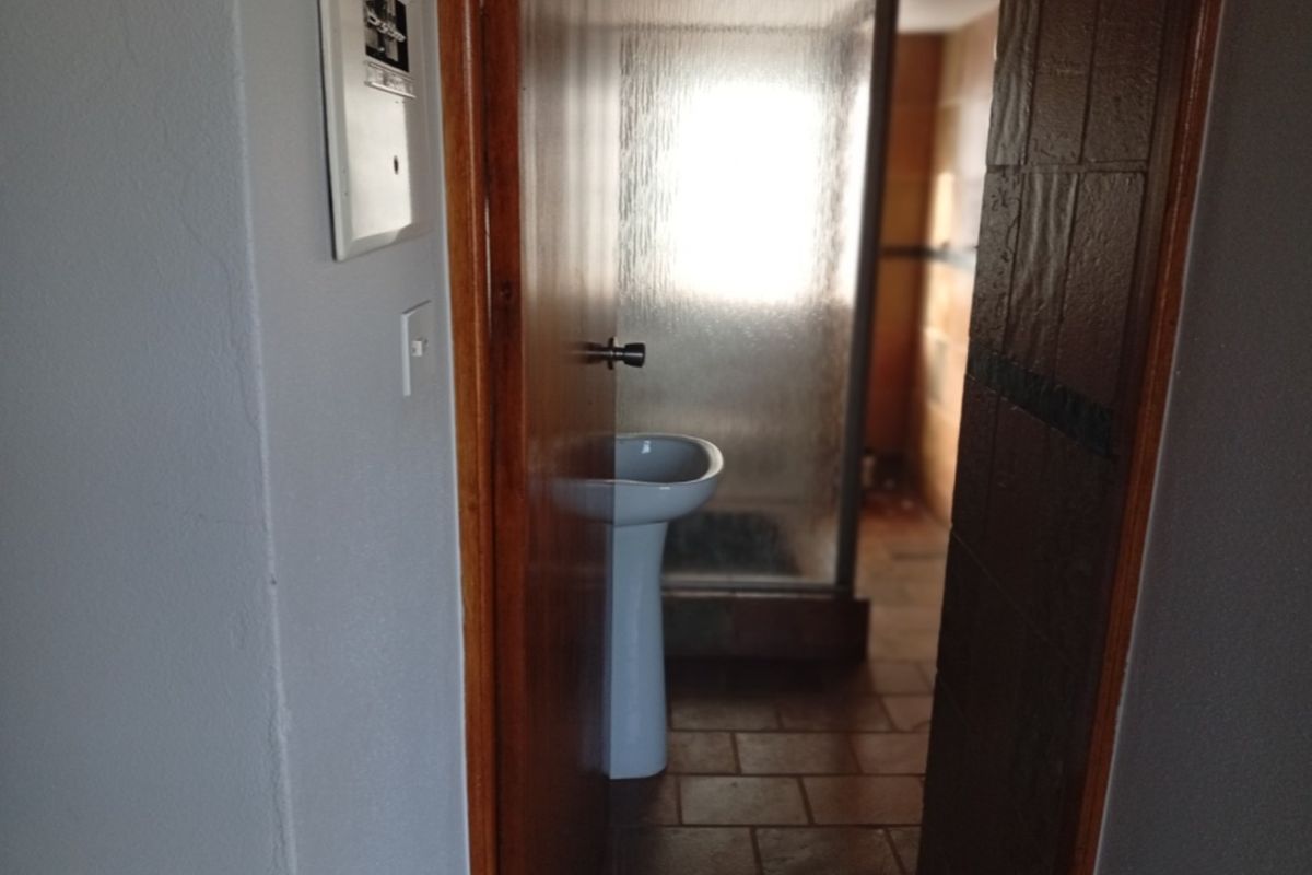 A view into a dated bathroom featuring a pedestal basin and a shower enclosure with tiled flooring.