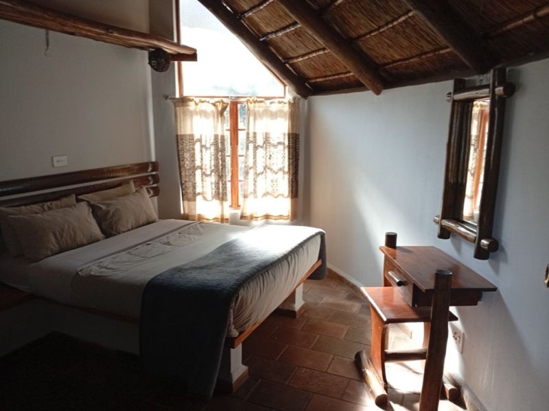 A rustic bedroom featuring a unique thatched roof with exposed timber beams and traditional terracotta tile flooring, creating a warm and cozy atmosphere.
