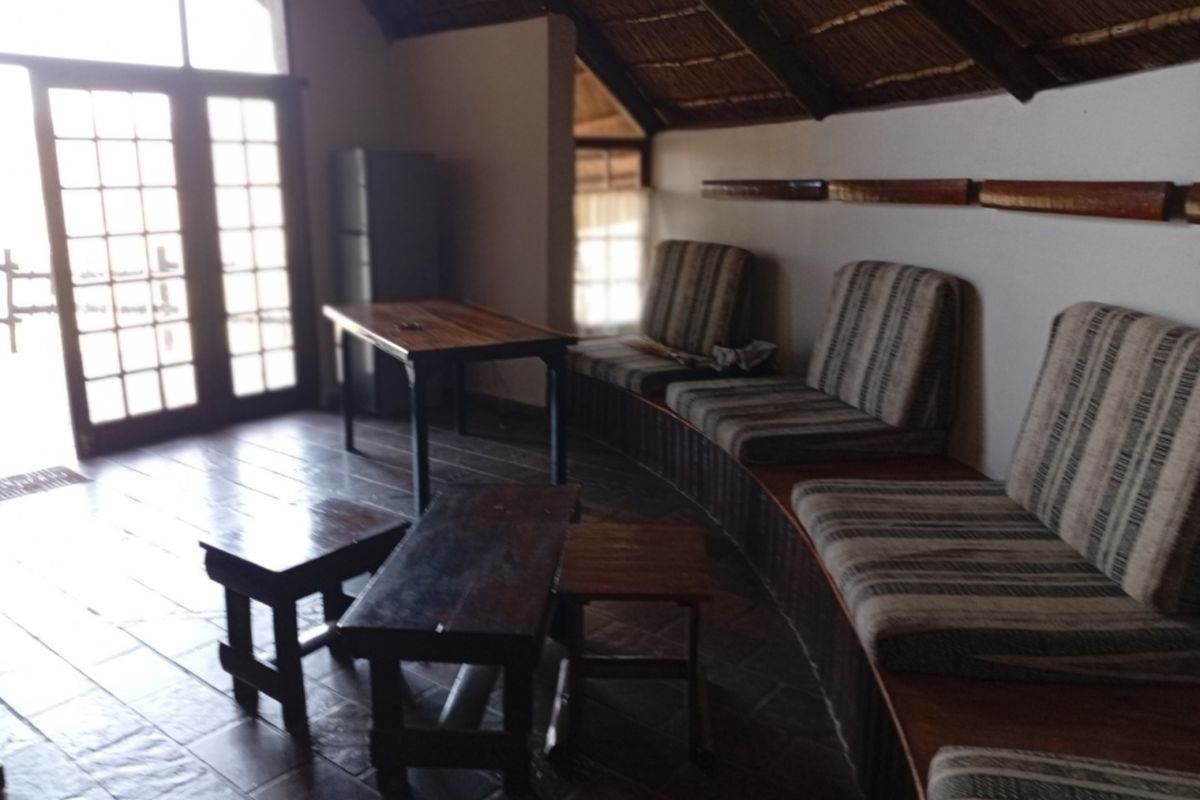 Living area featuring a rustic thatched roof with exposed timber rafters, tiled flooring, and built-in bench seating with access to an outdoor area.