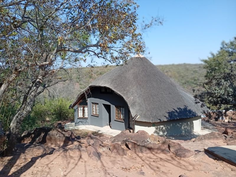 A charming thatched-roof cottage nestled in a natural, rocky landscape, featuring timber-framed windows and a solid exterior structure.