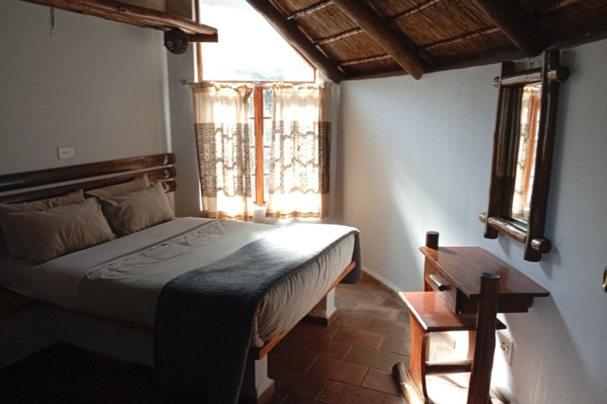 A rustic bedroom featuring a unique thatched roof with exposed timber beams and traditional terracotta tile flooring, creating a warm and cozy atmosphere.