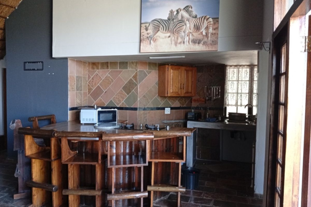 A rustic kitchen area featuring a built-in breakfast bar, stone tile backsplash, and wooden cabinetry with integrated hob and sink.