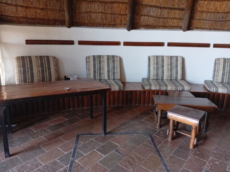 Covered patio area featuring a traditional thatched roof, built-in wooden bench seating, and durable stone tile flooring.