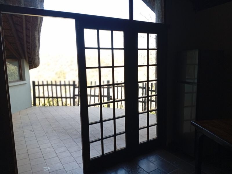 A view from an interior space looking out onto a tiled patio area with a wooden railing and thatched roof overhang.