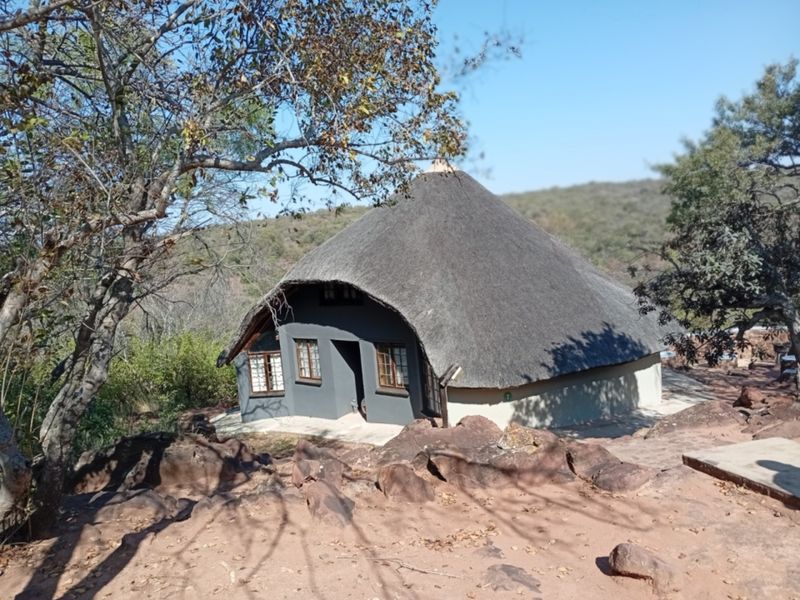 A rustic cottage featuring a traditional thatched roof and timber-framed windows, set within a natural rocky landscape.