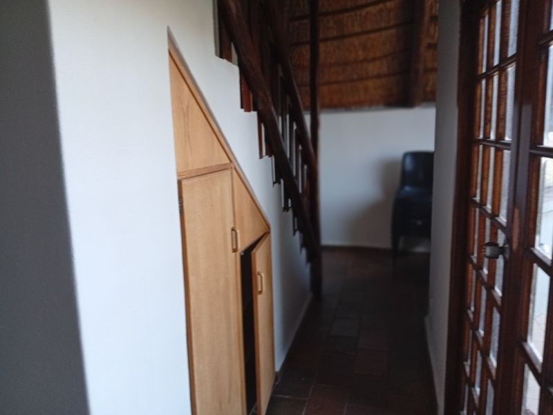 A hallway featuring under-stair storage cabinetry, a wooden staircase, and a timber-framed glass door leading to an adjacent space.