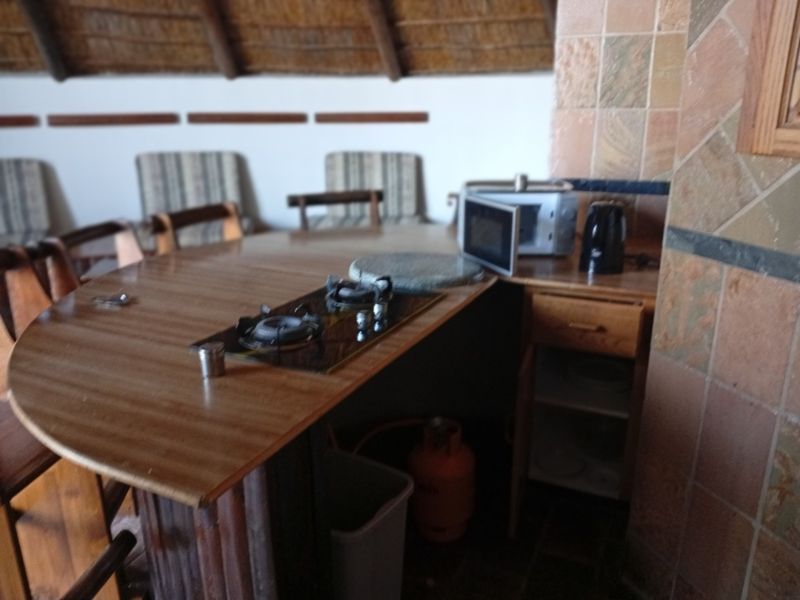 A dated kitchen area featuring a built-in gas hob, wooden cabinetry, and a traditional thatch roof ceiling.