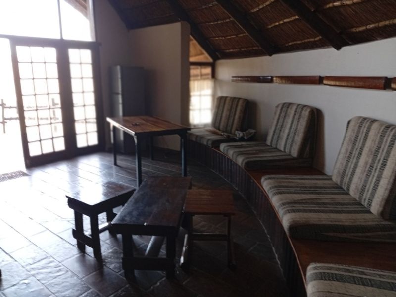 Living area featuring a rustic thatched roof with exposed timber rafters, tiled flooring, and built-in bench seating with access to an outdoor area.