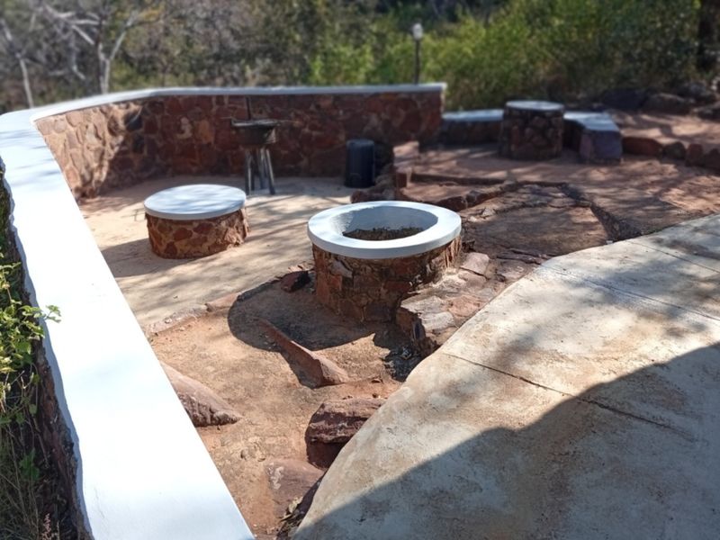 Outdoor patio area featuring a built-in stone fire pit, stone seating, and a stone retaining wall, set in a natural landscape.
