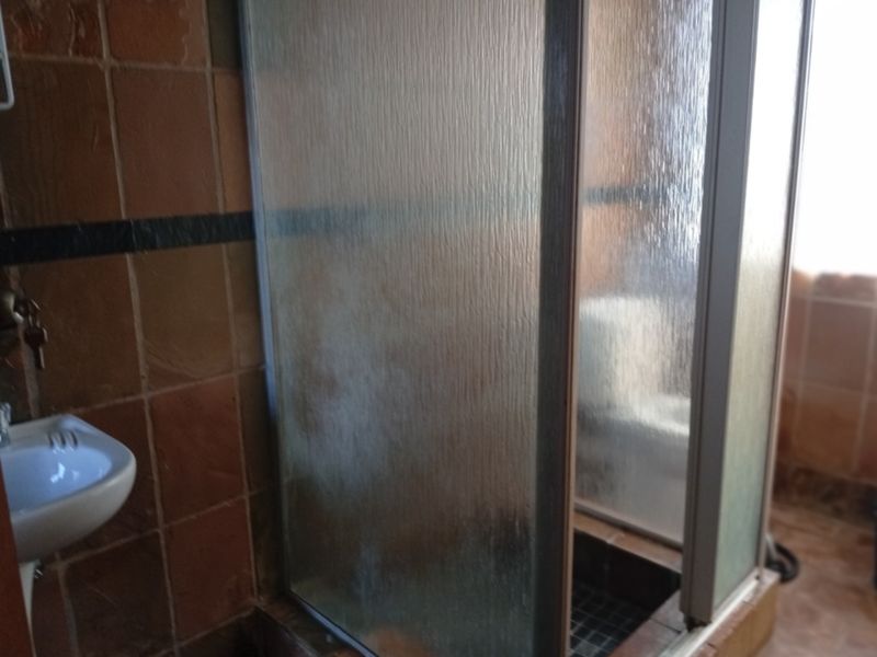 A dated bathroom featuring a shower enclosure and wall-mounted basin with terracotta-style wall tiling.